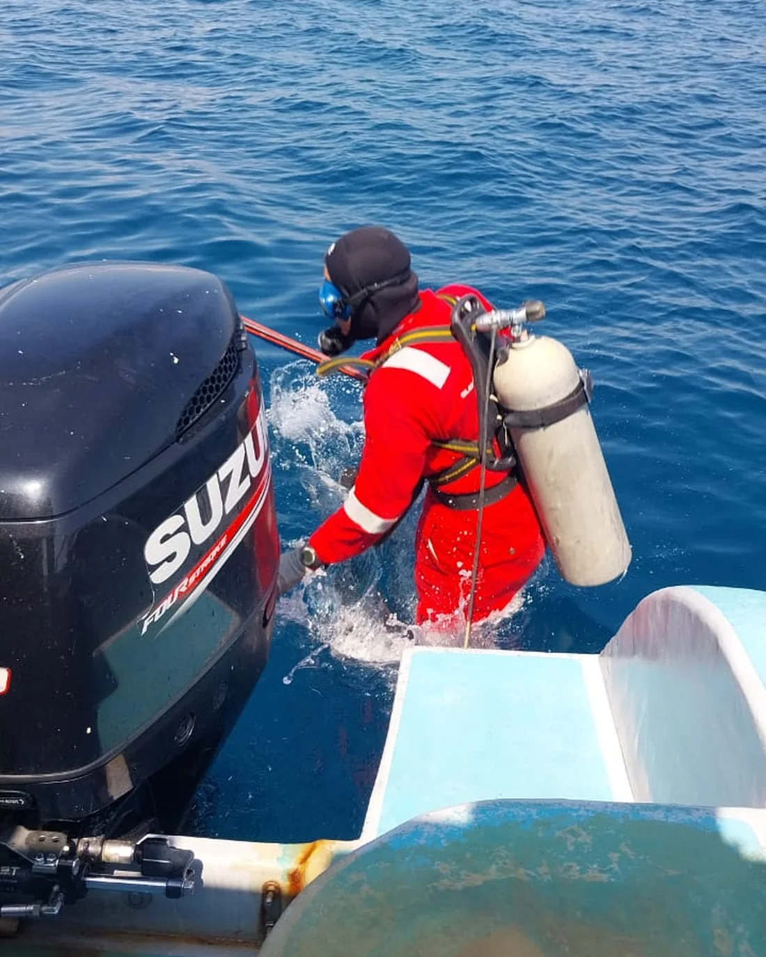 A diver in a survival suit entering the water from the dive boat