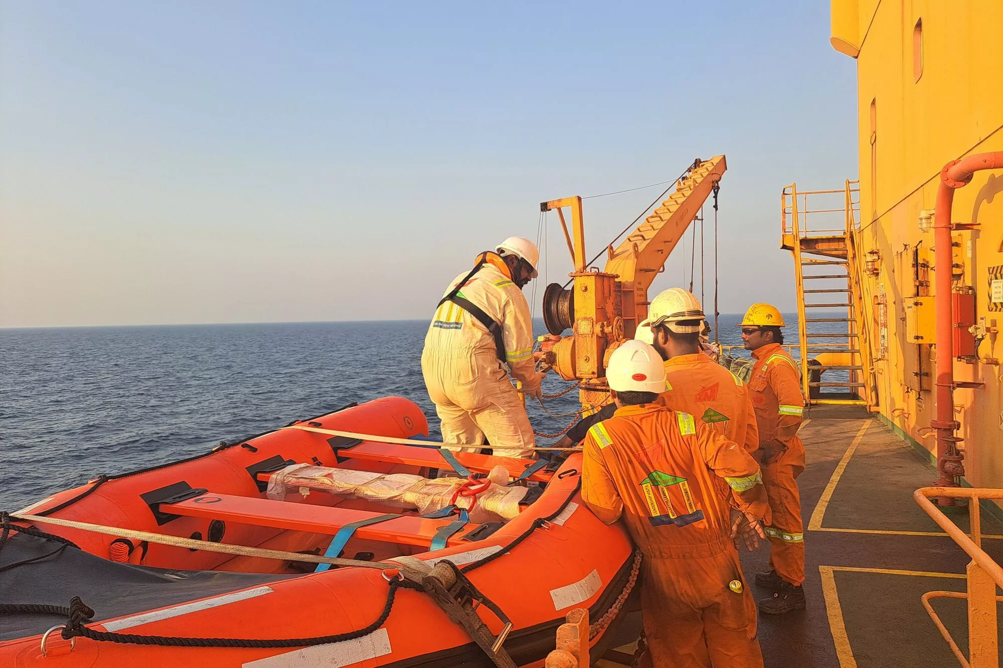Crew in orange coveralls working a vessel's deck at sea