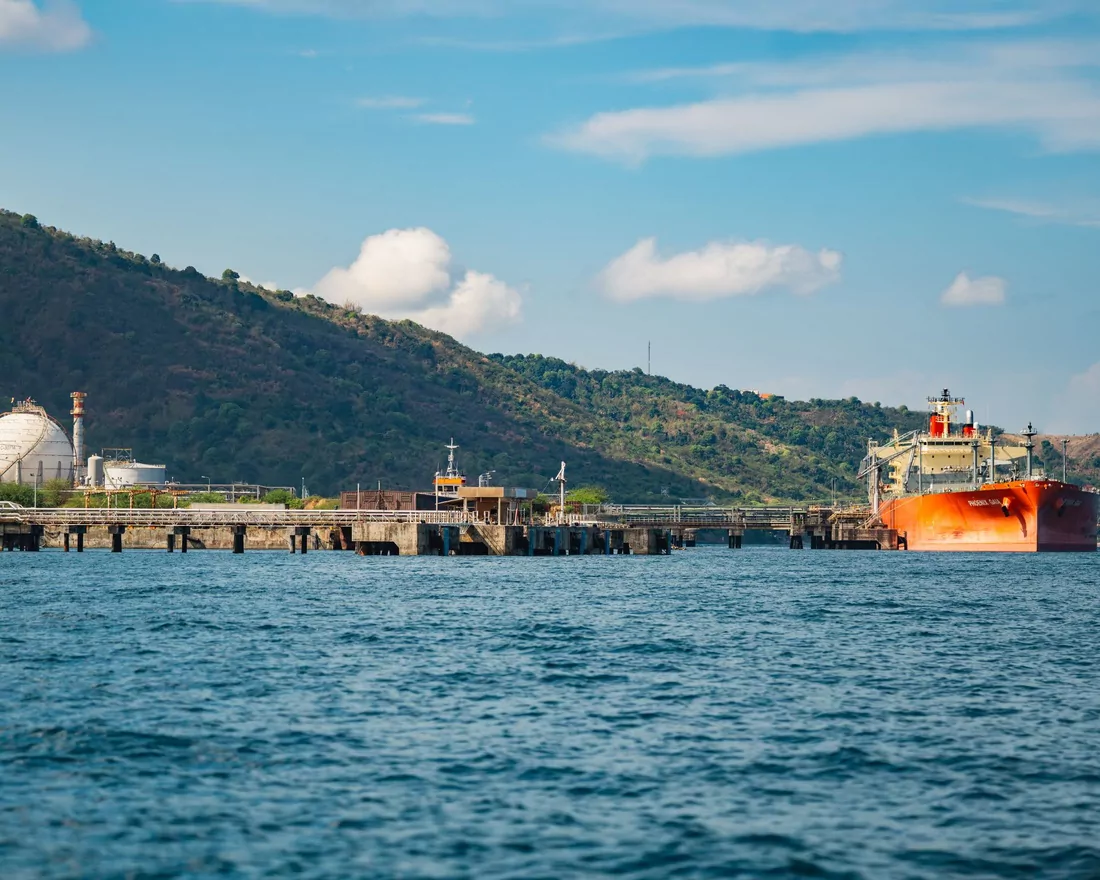 Refinery jetty and a berthed product tanker below forested hills