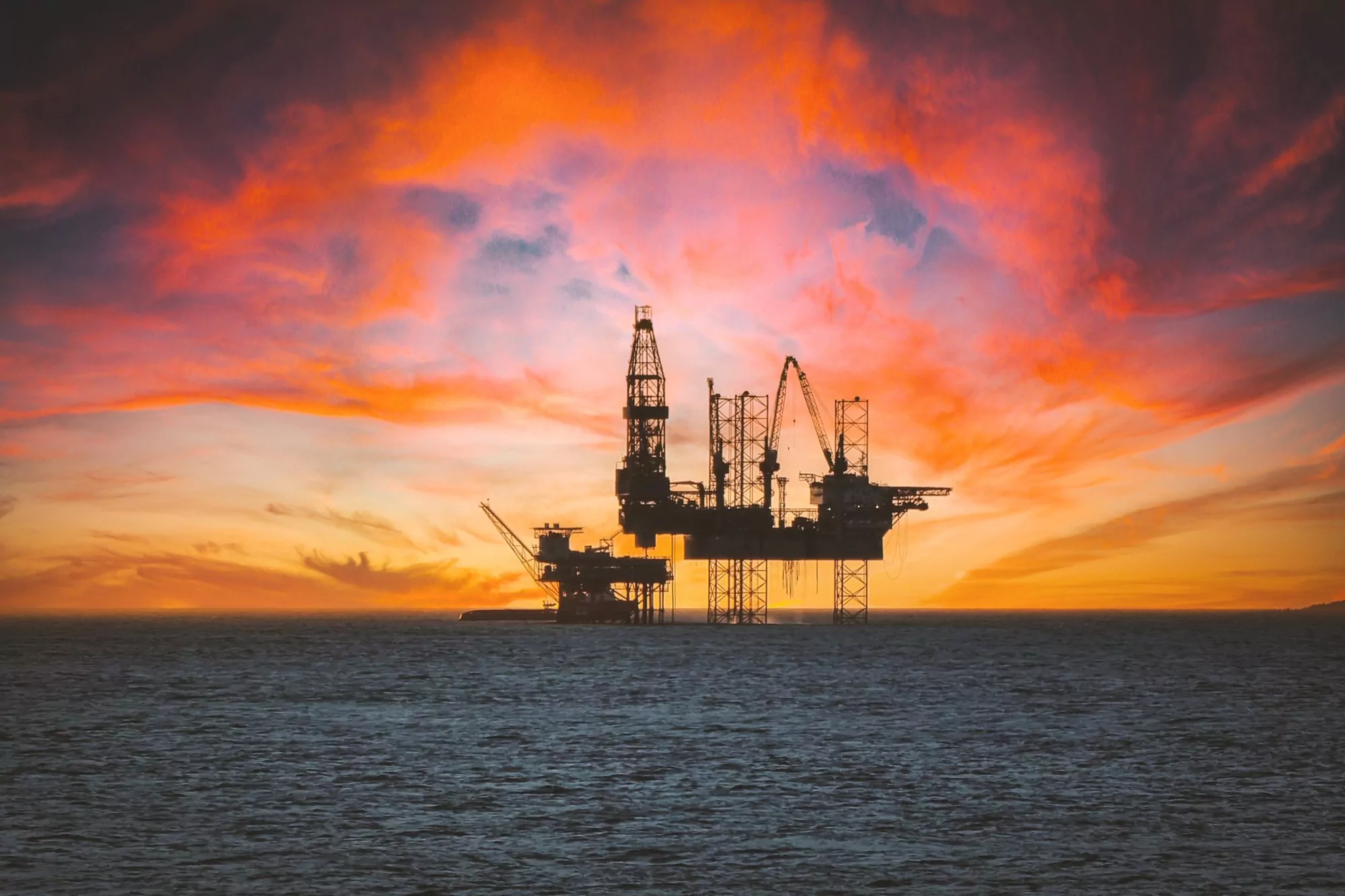 Offshore drilling rig standing on the horizon under a burning sunset sky