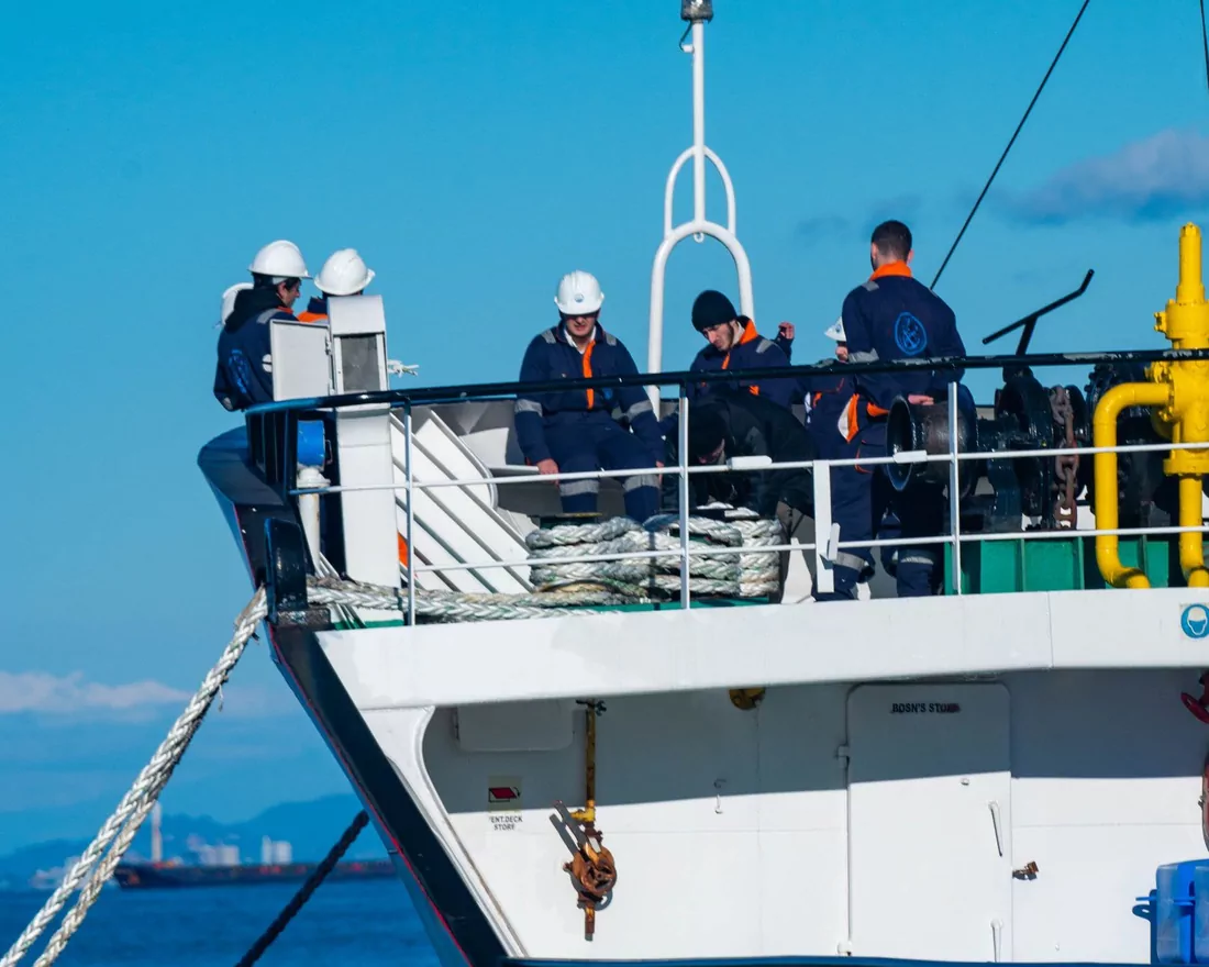 Mooring party in coveralls and hard hats working the forecastle of a vessel alongside