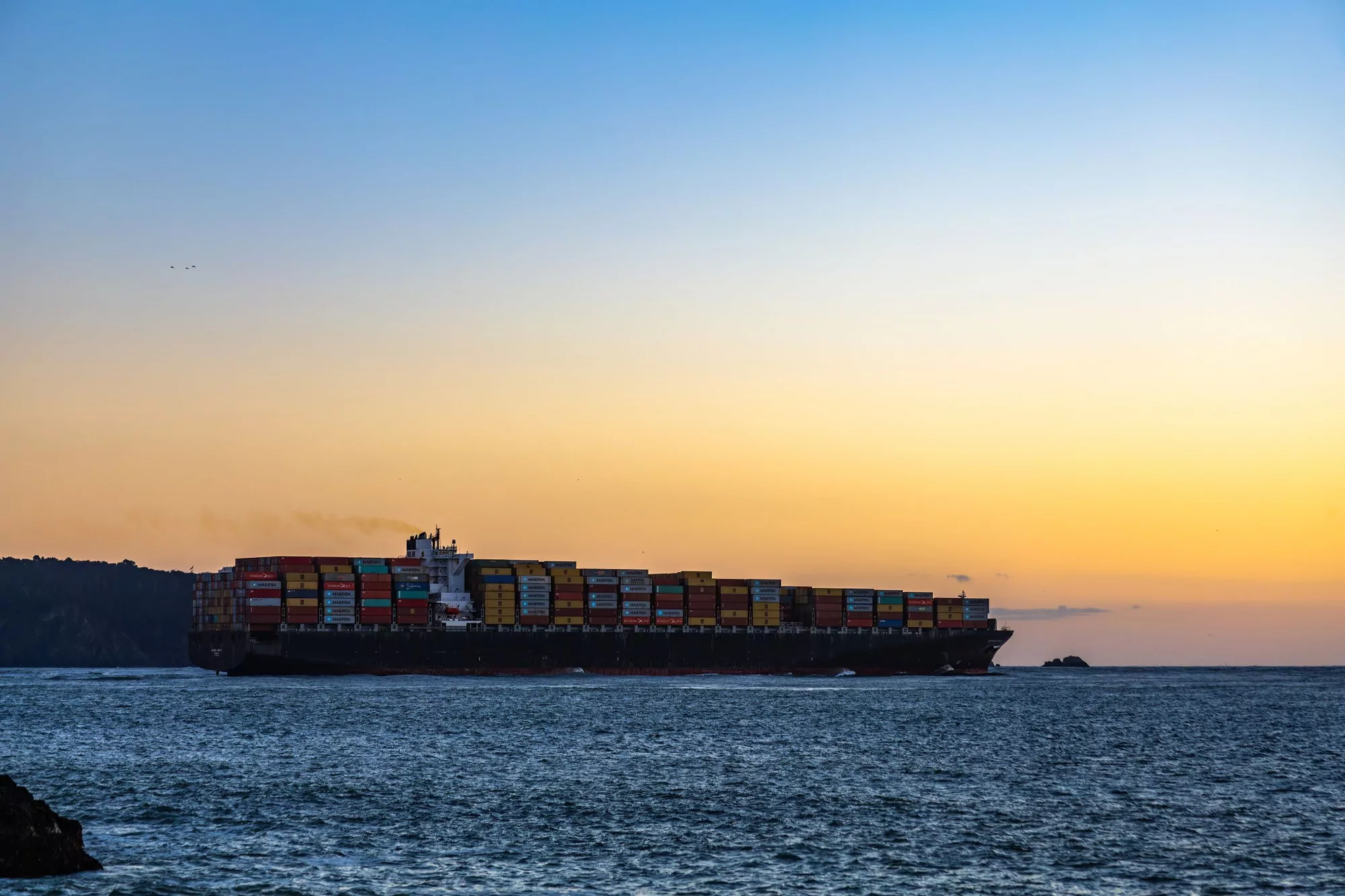 Loaded container vessel standing off a coastline at dusk