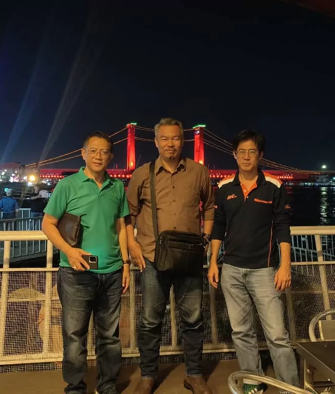 The Suria Crestway team with partners at the riverside in the evening, an illuminated bridge behind them