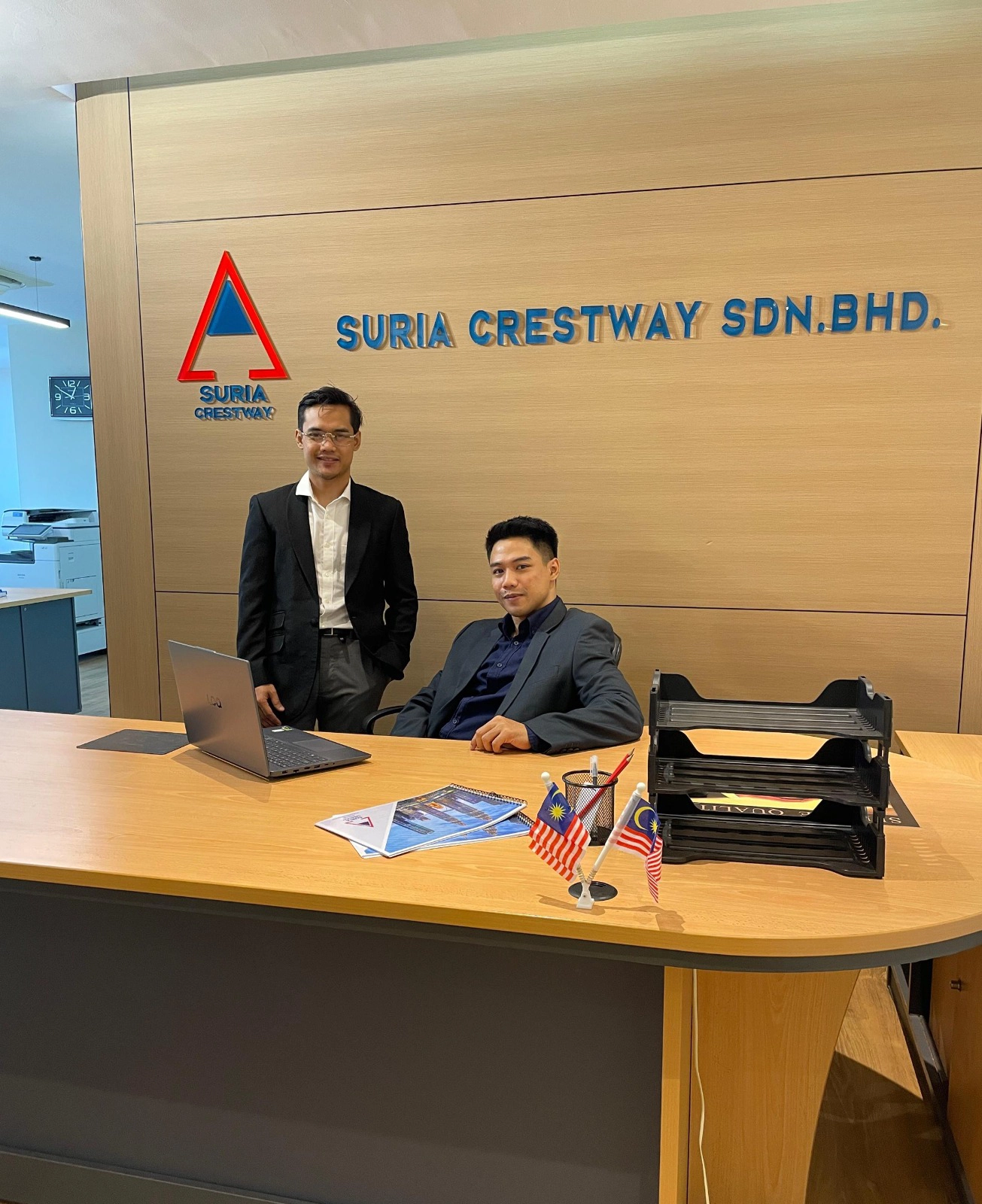 Two members of the Suria Crestway team at the office reception beneath the company signage